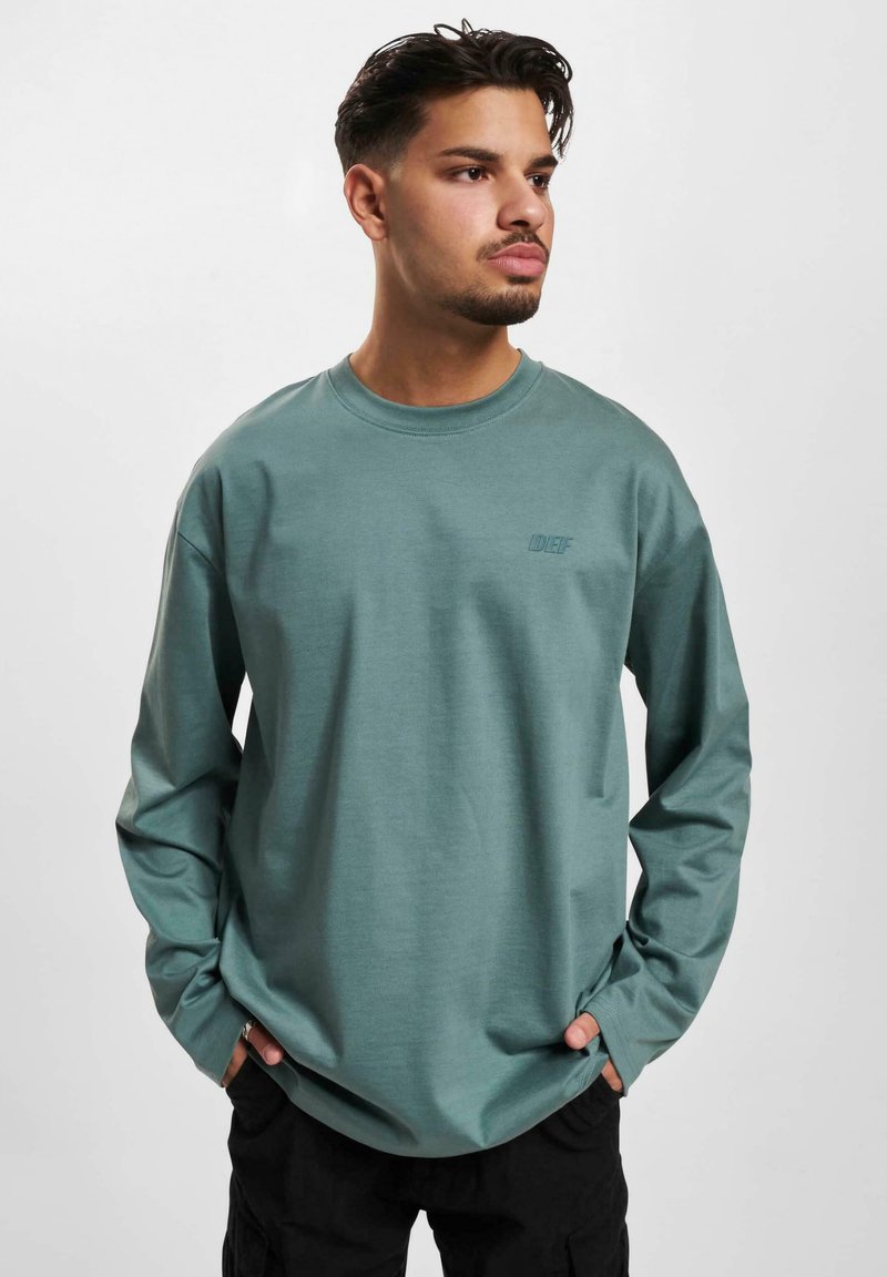 Long-sleeved, cotton-blend shirt in muted teal with a crew neckline and subtle logo detail on the chest.