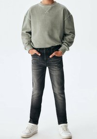 Sudadera gris de manga larga, combinada con jeans gris oscuro y zapatillas blancas. La sudadera tiene cuello redondo y puños de canalé.