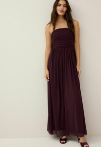 Trägerloses, knöchellanges Kleid in tiefem Burgunderrot mit gerafftem Oberteil und fließendem Rock, aus glattem Stoff gefertigt. Veredelt mit schwarzen High Heels.