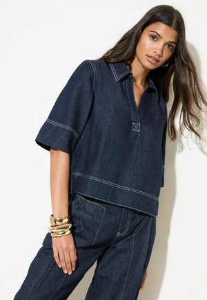 Dark denim short-sleeve top with a collared neckline, contrasting white stitching, and a boxy shape, paired with matching pants.