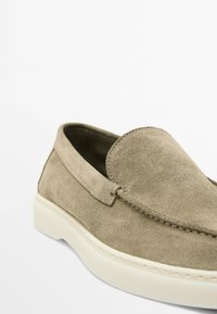 Beige suede slip-on shoe with a rounded toe, white rubber sole, and stitching accents along the edges.