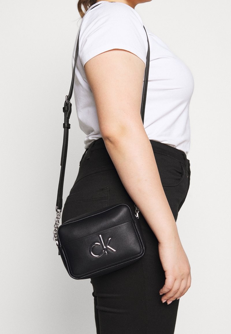 Sort læder crossbody taske med rektangulær form, sølvlogo og kædeprydet rem. Har en glat overflade og minimalistisk design.