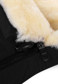 Zwart fabric met een gestructureerde buitenkant, voorzien van een crèmekleurige nepbontvoering. Een zwarte rits en togglesluiting zijn zichtbaar.