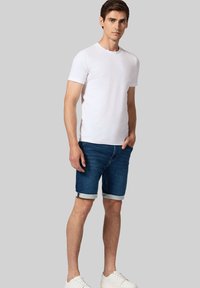 Biała koszulka z okrągłym dekoltem, dżinsowe szorty z podwiniętymi mankietami i białe trampki. Szorty mają klasyczny krój i niebieski kolor.