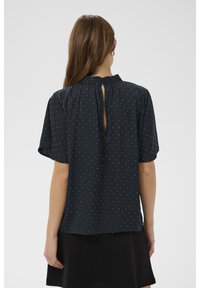 Blusa a maniche corte, blu scuro con pois bianchi, chiusura posteriore a goccia e vestibilità comoda. Realizzata in tessuto leggero.