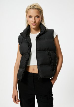 Smanicato imbottito nero con collo alto, chiusura frontale con zip e due tasche laterali. Realizzato in tessuto liscio, presenta sezioni trapuntate orizzontali.