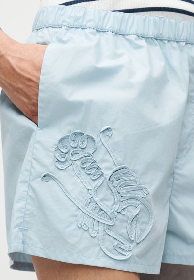 Ανοιχτό μπλε σορτς κατασκευασμένο από απαλό ύφασμα, με κεντητό σχέδιο αστακού στο πλάι, ελαστική μέση και πλαϊνή τσέπη.