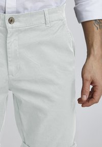 Pantalones de algodón de color claro con una textura suave, que cuentan con un cierre de botón y bolsillos laterales. Puños enrollados con un detalle mínimo.