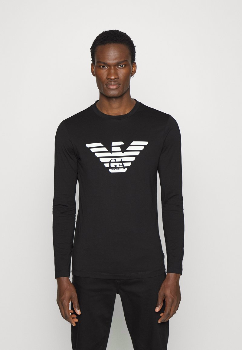 Svart långärmad T-shirt med en vit örnlogotyp och horisontella ränder vid bröstet, tillverkad av mjukt tyg med en figurnära design.