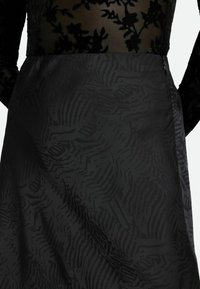 Schwarzes Kleid mit einem transparenten schwarzen Oberteil, das florale Muster aufweist, und einem strukturierten Satinrock mit einem subtilen zebraähnlichen Design.