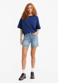 Sudadera de gran tamaño en color azul marino con mangas cortas, combinada con pantalones cortos de mezclilla en azul claro. Usada con zapatillas deportivas negras y calcetines blancos.