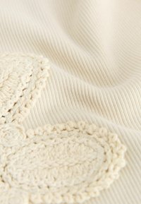 Cream-colored ribbed fabric with intricate crochet floral patterns in matching thread, showing texture and detail of the material.