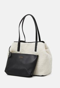 Sac fourre-tout noir en cuir synthétique avec un extérieur en fausse fourrure texturée crème et deux longues poignées. Il comprend une pochette noire amovible avec un accent en logo doré.