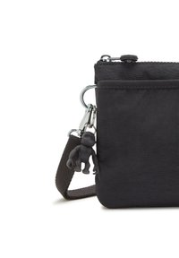 Borsa a tracolla nera in tessuto con chiusura a zip, cinturino rimovibile e un piccolo portachiavi a forma di scimmia attaccato. Forma rettangolare compatta, materiale testurizzato.