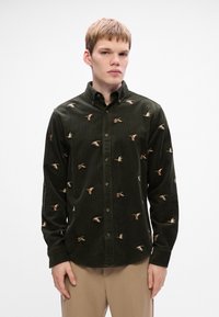 Mørkegrøn fløjlsskjorte med farverigt broderede ænder, krave med knapper og lange ærmer med knappede manchetter.