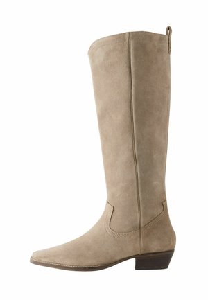 Botte en suede beige, hauteur genou, à bout pointu, avec des accents de couture subtils et un petit talon block. Texture lisse, design minimaliste.