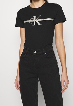 Czarny bawełniany t-shirt z metalicznym srebrnym logo i napisem na piersi, zestawiony z czarnymi, wysokim stanem, dżinsowymi spodniami.