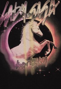 Svart t-skjorte med en rosa og lilla enhjørning silhuett med en teksturert manke, omkranset av et sirkulært design og stjerner, teksten lyder "LADY GAGA BORN THIS WAY."