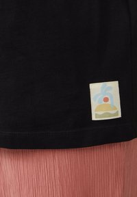 Czarny bawełniany t-shirt z kwadratową, kremową metką z kolorową grafiką burgera i kroplami wody w pobliżu dołu.