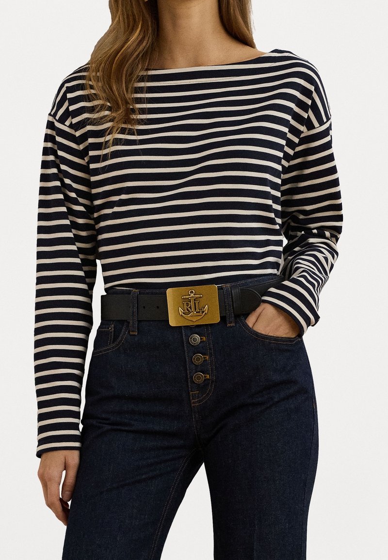 Camisa de rayas azul marino y crema de manga larga combinada con jeans oscuros de tiro alto; cinturón negro con hebilla de ancla dorada y botones.