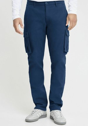 Marina byxor gjorda av hållbart tyg; har två stora sidofickor, slim fit och en knappstängning i midjan. Matchas med vita sneakers.