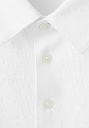 Camisa blanca con cuello y tres botones visibles, mostrando tela texturizada y ojales cuidadosamente cosidos en la tapeta frontal.