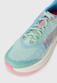 Baskets de course bleu clair avec un dessus en maille lisse, des accents roses et des motifs texturés. Comprend des lacets et une semelle rembourrée.
