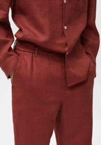 Red linen shirt with a button front, paired with matching linen pants featuring an elastic waistband and side pockets. Textured finish visible.