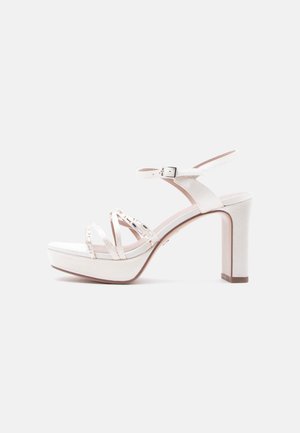 White high-heeled sandal with wide front strap, multiple thin straps, buckle closure, and textured platform. Block heel design.
