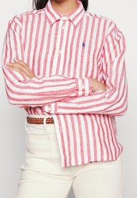 Camisa de botones a rayas rojas y blancas con collar clásico, hecha de un tejido ligero. Logo bordado notable en el pecho y mangas con puños.