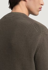 Suéter de punto verde oscuro con un patrón texturizado, cuello redondo y acentos de canalé en los hombros y el dobladillo. Acabado suave.