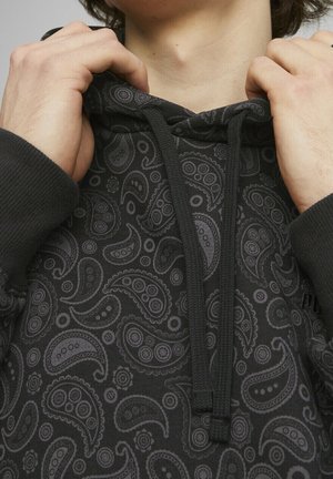 Sudadera con capucha negra con un estampado de paisley en tonos grises, con capucha ajustable mediante cordón y puños acanalados. Se aprecia una tela texturizada.