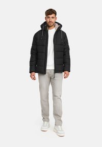 Giubbotto a vento nero con zip frontale, cappuccio e lacci grigi. Abbinato a jeans grigi chiari e sneakers bianche, con un interno testurizzato.