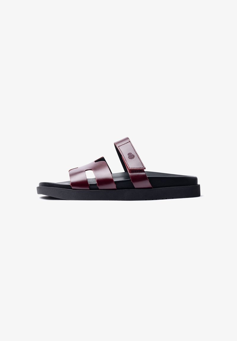 Maroon leather sandals with two wide straps, featuring cutout designs. Black rubber sole, flat profile, and embossed logo detail.