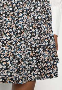 Schwarz-blumiger Rock mit taillierter Taille, der kleine weiße, rosa und blaue Blumen auf einem strukturierten Stoff zeigt. Faltendesign mit geschichteten Details.