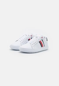 Weiße Sneaker mit zwei horizontalen Streifen in Rot und Schwarz. Hergestellt aus glattem Material, mit einer Schnürung und flacher Gummisohle.