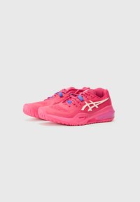 Des chaussures de sport roses avec une tige en mesh, des lacets bleus contrastés et des accents de logo blancs. Elles disposent d'une semelle texturée pour une meilleure adhérence et stabilité.