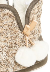 Zapatilla de punto texturizada en beige y marrón con pompones blancos de felpa y un acento de cinta color beige, que cuenta con un forro suave y una suela resistente.