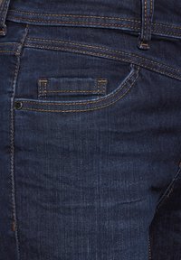 Mörkblå denimjeans med en standard bakficka med orange sömnad och en liten ficka för klocka ovanför. Slät textur, figursydd design.