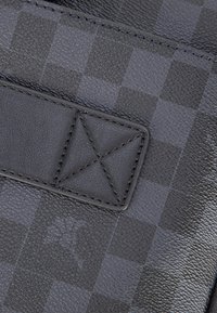 Black textured leather featuring a checkered pattern, with a black leather strap and stitched triangular detail. Smooth and durable finish.