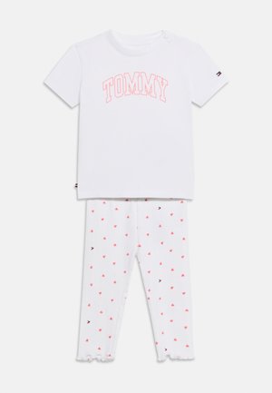 Ensemble pour tout-petit blanc comprenant un haut à manches courtes avec l'inscription « TOMMY » en rose et des leggings blancs assortis avec de petits motifs de cœurs roses.