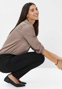 Blusa taupe de manga larga con textura suave, pantalones negros ajustados y zapatos planos negros, mostrada en una posición de cuclillas.