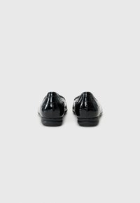 Chaussures en cuir verni noir avec une texture lisse et brillante et un petit talon. Bout arrondi avec des détails en surpiqûre sur le dessus.