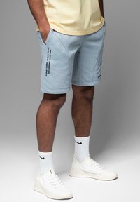 Lyseblå shorts lavet af blødt stof, med kontrastfarvet sort tekst på siden, i en afslappet pasform og med buede sømme.