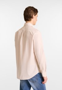 Lichtbeige longsleeve shirt met een gestructureerde kraag, een gladde textuur, rugplooidetail en knopenmanchetten, gecombineerd met blauwe jeans.