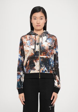 Cropped hooded jacket with a multicolored abstract pattern in black, orange, and blue, made of a velvety fabric, featuring a gold zipper.