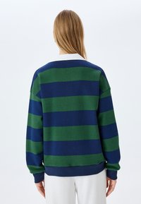 Zielono-granatowy sweter w paski o luźnym kroju, z prążkowanymi mankietami i dołem. Posiada białą kołnierzykową detal na plecach. Miękka tekstura materiału.