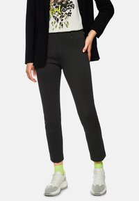 Black tailored pants with a slim fit, featuring front pockets, a smooth texture, and paired with white sneakers and neon green socks.