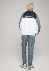 Joggedress i lysegrått og hvitt med en svart øvre del, med elastiske mansjetter og sidestriper, brukt sammen med sølvfargede treningssko.