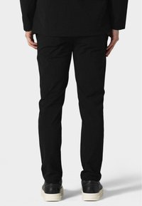 Fekete, slim fit nadrág, sima textúrával és finom varrási részletekkel, feketére festett cipővel és fehér talppal párosítva.
